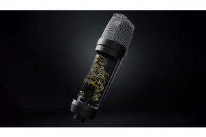 A close-up of the Rode NT1 5th generation microphone on a stand, with a blurry background of a recording studio setup.